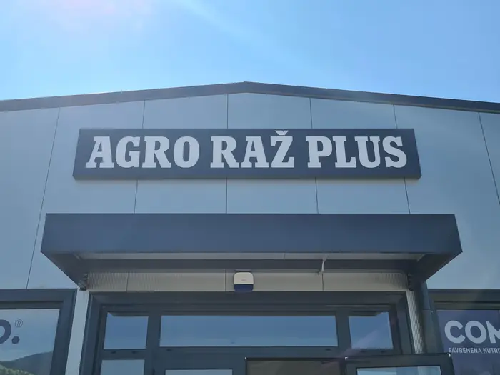 Bela 3D slova Agro Raž Plus na sivom panelu iznad ulaza u prodavnicu