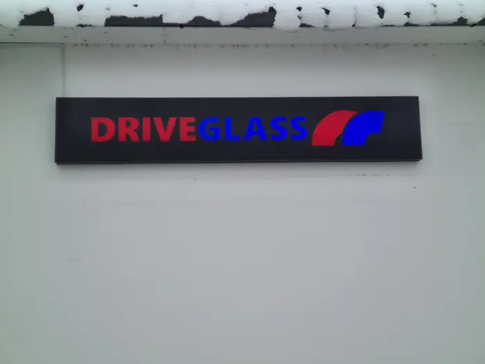 Reklamna tabla DriveGlass sa crvenim i plavim natpisom na crnoj podlozi