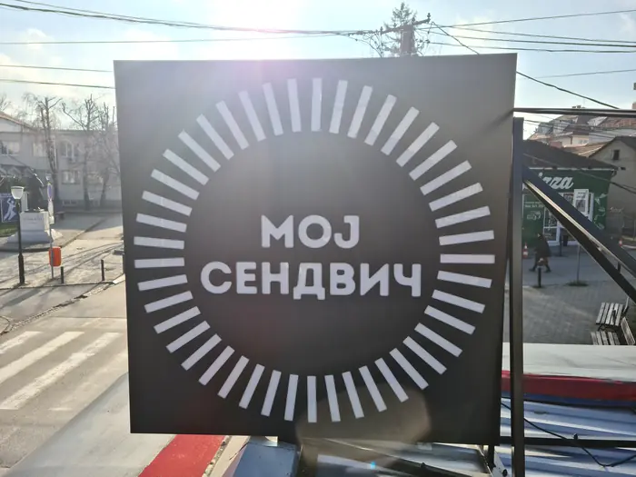 Reklamna tabla МОЈ СЕНДВИЧ sa isečenim zracima oko natpisa