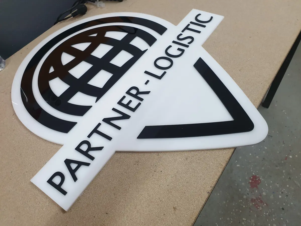 Logo izrezan iz belog klirita, položen na radni sto u radionici